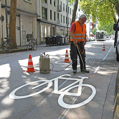 Winfried Hennen vom Trierer Bauunternehmen Franken bringt mit einem Gasbrenner eines von fünf Fahrradpiktogrammen auf die Fahrbahn der Bruchhausenstraße auf. Verbunden mit einem Richtungspfeil signalisieren sie, dass der Radverkehr gegen die Richtung der Einbahnstraße fahren darf.  