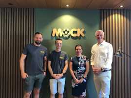 Vier Personen stehen vor einer Wand und dem Schriftzug "Mock". 