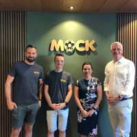 Vier Personen stehen vor einer Wand und dem Schriftzug "Mock". 