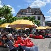 Menschen lauschen auf Sitzsäcken und Klappstühlen einer Lesung auf dem Domfreihof