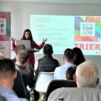 Die Amtsleiterin der Wirtschaft hält einen Vortrag vor Mitgliedern des Netzwerks "Attraktive Unternehmen Trier". Sie steht vor einer Projektion des Netzwerklogos.