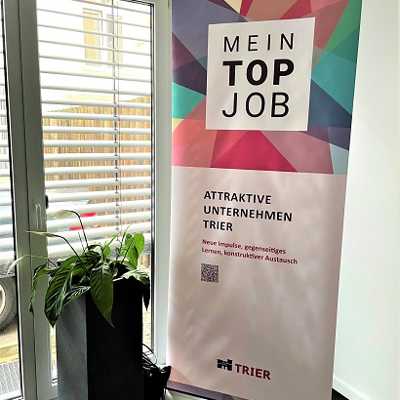 Das Rollup des Netzwerks "Attraktive Unternehmen Trier" steht neben einer Zimmerpflanze. Die Aufschrift des Rollups lautet "Mein Top Job".